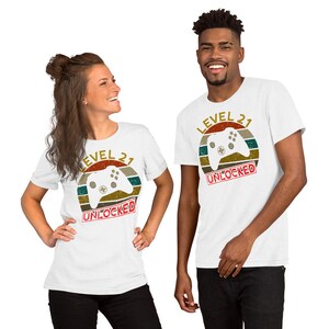 May include: Two white t-shirts with a retro-style graphic of a video game controller and the text "Level 21 Unlocked".