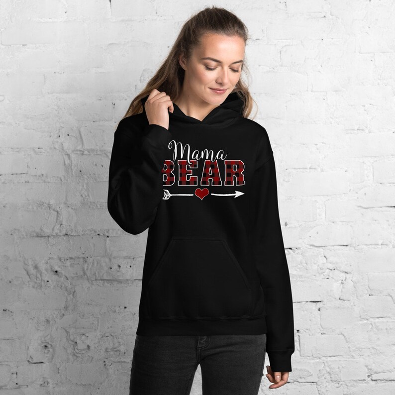 May include: Black hooded sweatshirt with the text "Mama Bear" in white letters with a red and black buffalo plaid pattern. A white arrow with a red heart is below the text.