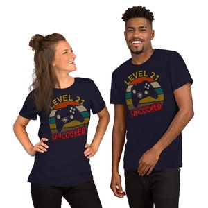 May include: Two people wearing navy blue t-shirts with a retro-style graphic of a video game controller and the text "Level 21 Unlocked".