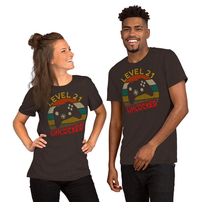 May include: Two people wearing dark brown t-shirts with a retro-style graphic of a video game controller and the text "Level 21 Unlocked".