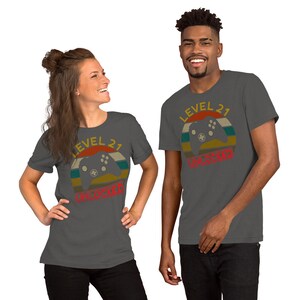 May include: Two people wearing charcoal gray t-shirts with a retro-style graphic of a video game controller and the text "Level 21 Unlocked".