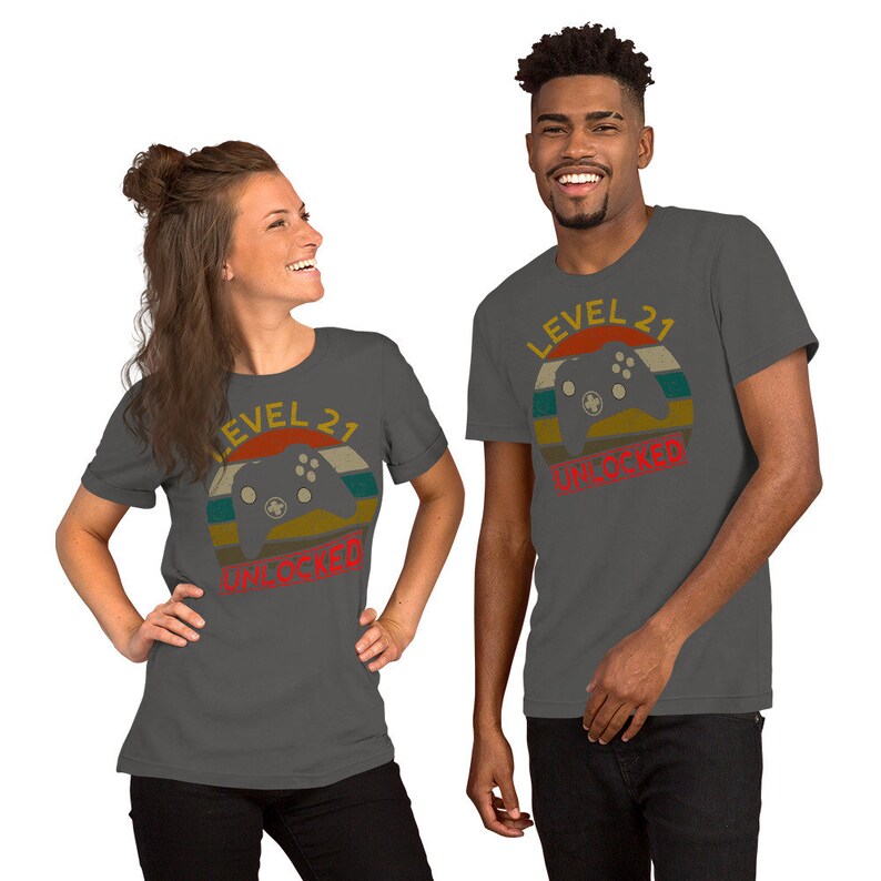 May include: Two people wearing charcoal gray t-shirts with a retro-style graphic of a video game controller and the text "Level 21 Unlocked".