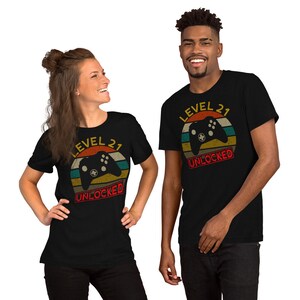 May include: Two people wearing black t-shirts with a retro-style graphic of a video game controller and the text "Level 21 Unlocked".