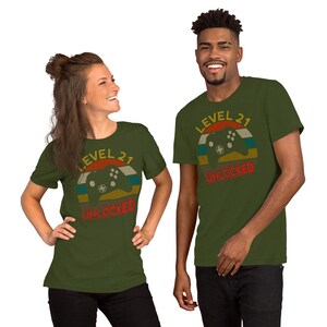 May include: Two people wearing green t-shirts with a retro-style graphic of a video game controller and the text "Level 21 Unlocked".