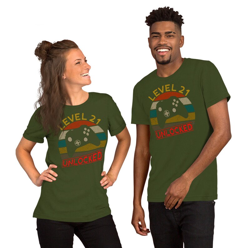May include: Two people wearing green t-shirts with a retro-style graphic of a video game controller and the text "Level 21 Unlocked".