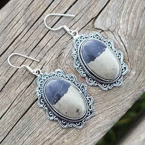 Può includere: Un paio di orecchini d'argento con una pietra nera e beige incastonata in una cornice d'argento decorata.