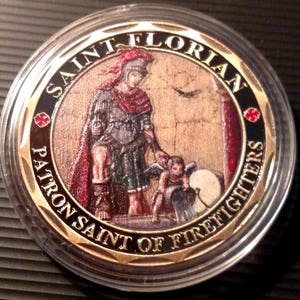 May include: A gold-colored coin with a black border and a red cross on each side. The coin features a painting of Saint Florian, a patron saint of firefighters, holding a bucket of water. The text "SAINT FLORIAN PATRON SAINT OF FIREFIGHTERS" is inscribed around the edge of the coin.