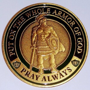 May include: A gold-colored round coin with a green and black border. The center of the coin features a gold-colored image of a Roman soldier holding a sword and shield. The text "PUT ON THE WHOLE ARMOR OF GOD" is written around the top of the coin, and the text "PRAY ALWAYS" is written around the bottom of the coin.