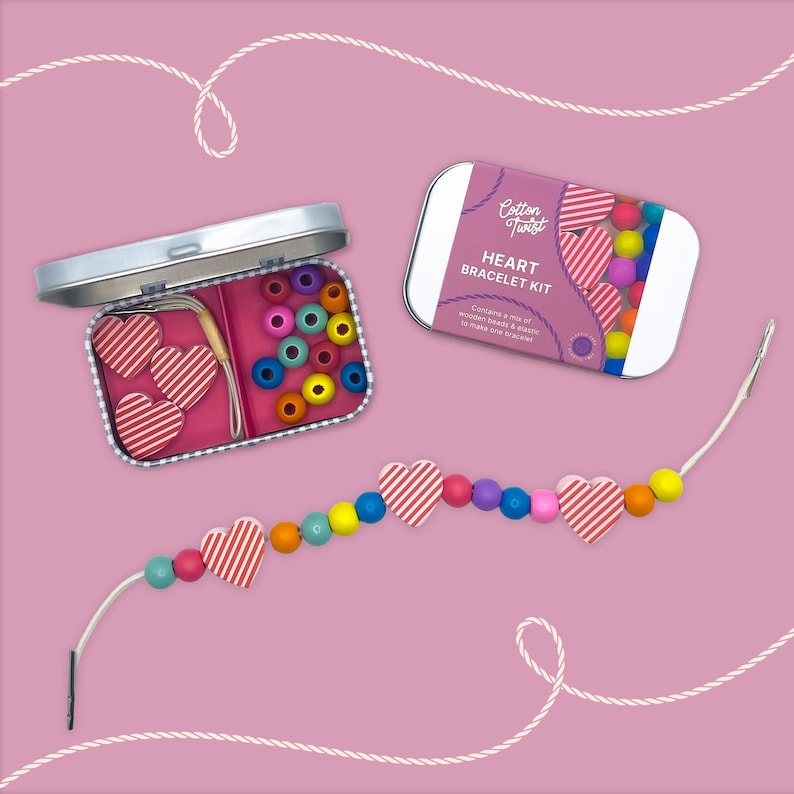 May include: A heart bracelet kit with a pink background. The kit includes a metal tin with beads and heart-shaped charms, and a partially strung bracelet. The text on the tin reads "Cotton Twist HEART BRACELET KIT".