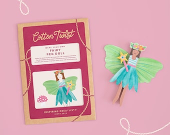 Puede incluir: Un kit de muñeca de hadas con una muñeca terminada y embalaje. El kit incluye una caja de cartón marrón con el texto "Cotton Twist" y "Make Your Own Fairy Peg Doll". La muñeca tiene alas verdes y un vestido azul.