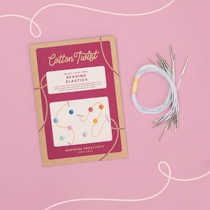 Puede incluir: Un kit de manualidades Cotton Twist Make Your Own Beading Elastics en un paquete rectangular de cartón con un centro magenta y bordes marrones, que incluye texto e ilustraciones, junto a un manojo de cordones elásticos blancos con puntas metálicas.