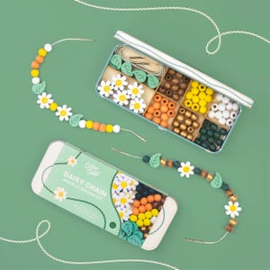 Può includere: Un kit per creare braccialetti Daisy Chain in una scatola di latta azzurra. Il kit include perline di legno di vari colori, perline a forma di margherita e foglia, e filo. È incluso anche un braccialetto parzialmente assemblato.