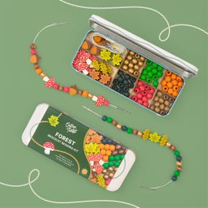 May include: A Forest Bracelet Beading Kit with wooden beads and elastic. The kit includes a variety of colorful beads, including acorns, mushrooms, and leaves. The kit is in a metal tin with the text "Forest Bracelet Beading Kit".