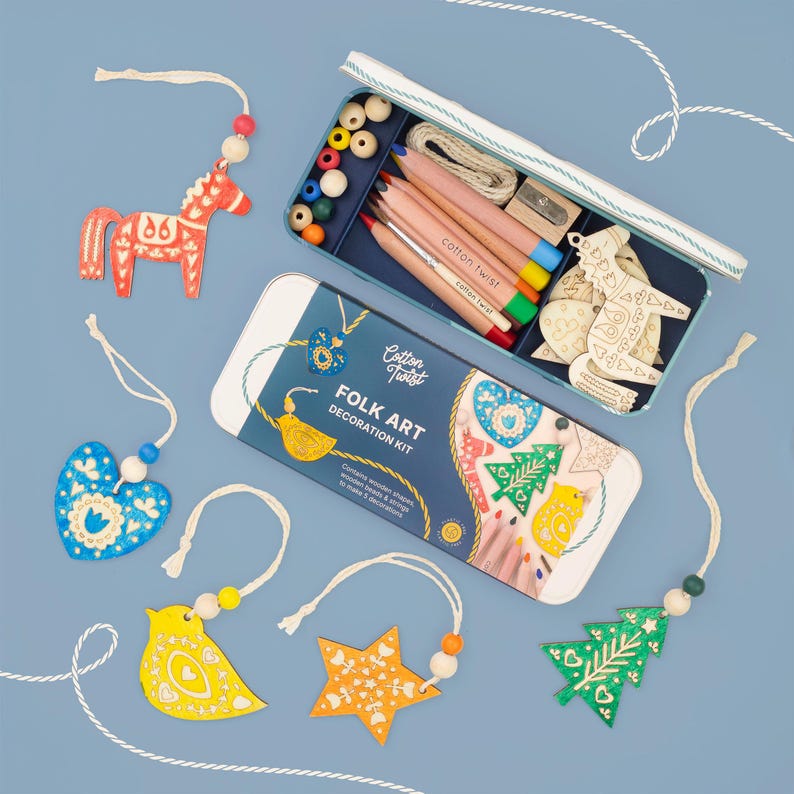 May include: A Folk Art Decoration Kit in a rectangular tin featuring wooden shapes, colored pencils, beads, and string. The kit includes a red horse, blue heart, yellow bird, orange star, and green tree ornament, all with intricate white patterns.