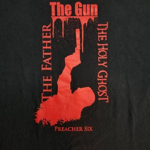 May include: Black t-shirt with red text and graphic. The text reads "The Gun", "The Holy Ghost", "The Father", and "Preacher Six". The graphic is a silhouette of a person holding a gun.