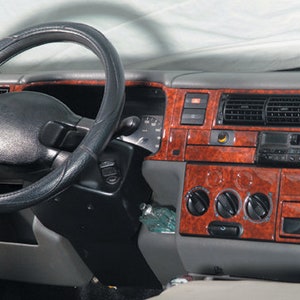 May include: A black leather steering wheel with a woodgrain dashboard in a car interior. The dashboard has a radio, air vents, and control knobs.