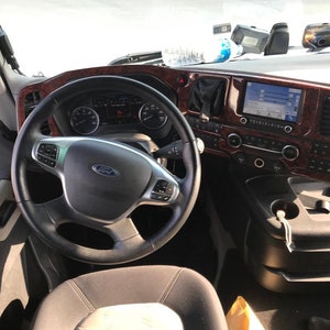 May include: A close-up view of the interior of a truck cab. The steering wheel is black leather with a silver Ford logo. The dashboard is brown wood-grain with a black screen and buttons.