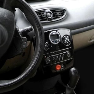 Puede incluir: Interior de coche con volante negro, salpicadero y palanca de cambios. El salpicadero es negro brillante con detalles plateados, incluyendo rejillas de ventilación y paneles de control. Un botón rojo brillante es visible.