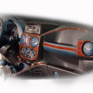 Puede incluir: Un salpicadero de vehículo con un volante gris oscuro, una consola central con acabado de veta de madera, rejillas de ventilación circulares, una radio y mandos de climatización. El texto ARS cockpit design es visible en la parte inferior.