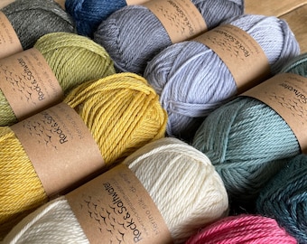 May include: A collection of yarn skeins in various colors, including green, yellow, gray, blue, white, pink, and teal. Each skein has a brown paper label with the text "Rock & Saltwater" and "Merino Silk - dk weight".