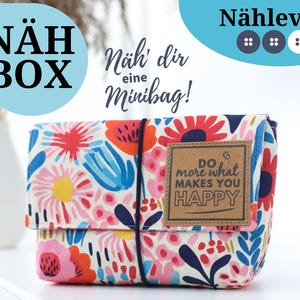 Könnte beinhalten: Eine weiße Stofftasche mit einem Blumendruck in den Farben Rosa, Rot, Blau und Gelb. Die Tasche hat einen Klappverschluss und ein braunes Lederpatch mit dem Text "Do more what makes you happy".