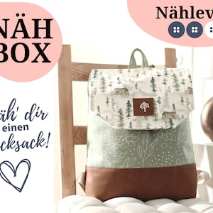 Könnte beinhalten: Ein grüner und brauner Stoffrucksack mit Waldmotiv. Der Rucksack hat eine Klappe mit einem kleinen, aus Holz geschnittenen Baum. Der Text "Näh' dir einen Rucksack!" ist auf dem Bild zu sehen. Der Text "Nählevel" ist ebenfalls auf dem Bild zu sehen.