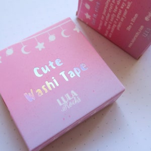 Puede incluir: Caja rosa con un dise&ntilde;o hologr&aacute;fico que presenta el texto "Cute Washi Tape" y el nombre de la marca "LULA Rocks".