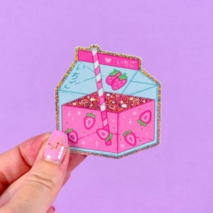 May include: A pink and blue glitter sticker of a milk carton with a straw and strawberries inside. The carton has Japanese text that says "いちごみるく" which translates to "strawberry milk".