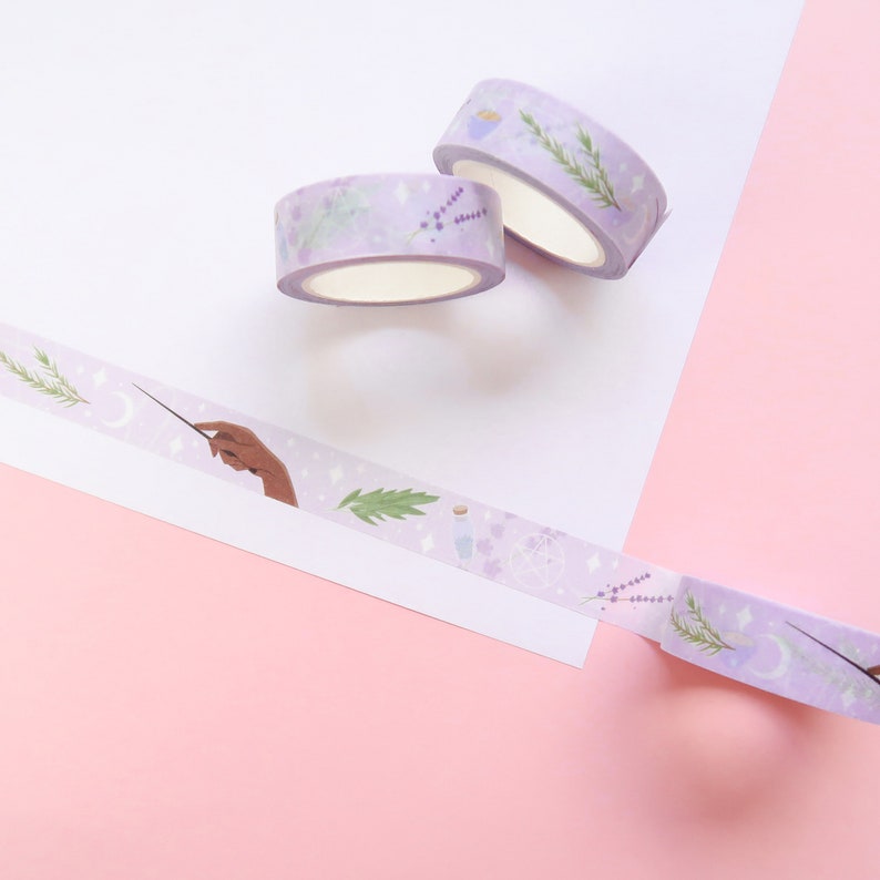 Puede incluir: Dos rollos de cinta washi morada con un tema m&aacute;gico. Un rollo presenta una mano sosteniendo una varita, estrellas y ramitas de lavanda. El otro rollo presenta una botella de poci&oacute;n, una luna creciente y un pentagram.