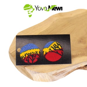 Puede incluir: Un par de pendientes redondos con un diseño de estampado africano colorido. Los pendientes tienen un fondo azul, amarillo y rojo con ramas de árboles negras.