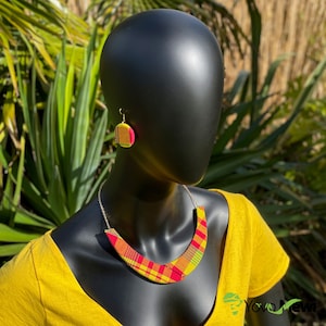 Peut inclure: Un collier et des boucles d'oreilles assorties en tissu à motifs jaunes, rouges et verts. Le collier est de forme incurvée et les boucles d'oreilles sont rondes.