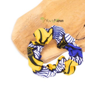 Può includere: Un elastico per capelli scrunchie con motivo giallo, blu e bianco. Lo scrunchie è realizzato in tessuto e ha un aspetto raccolto.