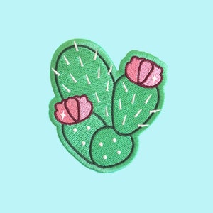 Peut inclure: Un patch brodé de cactus vert avec des fleurs roses. Le cactus a des épines blanches et est bordé de blanc.