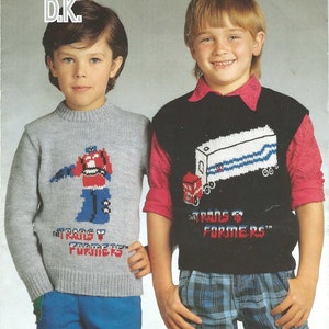 May include: Two children wearing knitted sweaters with a Transformers theme. The sweaters are gray and black with a red, blue, and white graphic of a robot and a truck. The text "The Transformers" is printed on both sweaters.