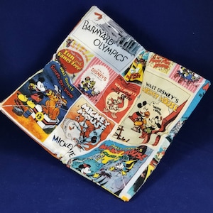 May include: A colorful fabric square with a patchwork design featuring Mickey Mouse and other Disney characters. The fabric includes the text "Barnyard Olympics", "Walt Disney's Mickey Mouse", "Mickey Mouse", "Walt Disneys", "Society Do: Show", and "Fancy Free".