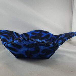 May include: A blue and black fabric bowl with a flame pattern. The bowl is folded and appears to be made of a soft material.