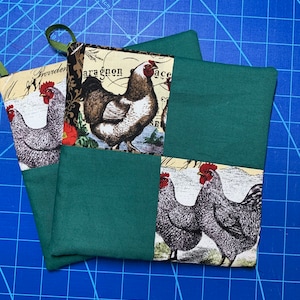 May include: Two green and cream fabric pot holders with a rooster design. The fabric is a patchwork of green and cream squares with a rooster design in each square. The text "Garden" is visible on one of the pot holders.