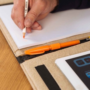 May include: A beige felt portfolio with a white notepad, an orange highlighter, a yellow pencil, and a white tablet with a black screen displaying various apps.
