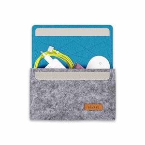 Könnte beinhalten: Eine graue Filztasche mit blauer Filz-Innenausstattung und einem braunen Lederanhänger mit der Aufschrift "RAVARE". Die Tasche ist geöffnet und enthält ein weißes Ladegerät, ein gelbes Ladekabel und eine weiße kabellose Maus.