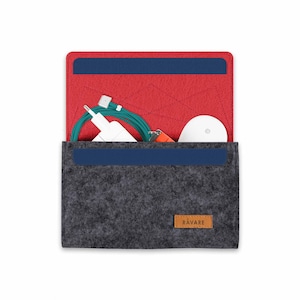 Könnte beinhalten: Eine graue Filztasche mit roter Filzfütterung und blauem Besatz. Die Tasche ist geöffnet und enthält ein weißes Ladegerät, ein grünes Ladekabel, einen weißen kabellosen Ohrhörer und einen roten USB-Stick. Die Tasche hat ein braunes Leder-Etikett mit dem aufgedruckten Wort "RAVARE".