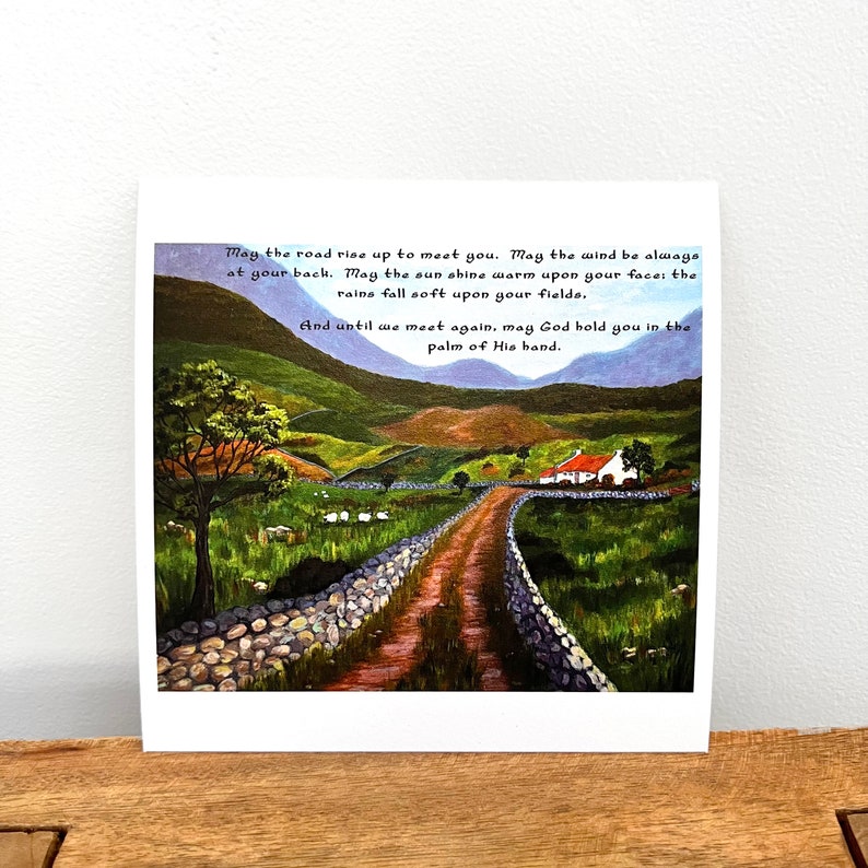 Puede incluir: Una pintura de acuarela de un camino sinuoso que conduce a una peque&ntilde;a caba&ntilde;a blanca con un techo rojo. El camino est&aacute; bordeado por muros de piedra y hierba verde. La pintura tiene una cita sobre el camino que se eleva para encontrarte, el viento que te da la espalda, el sol que brilla c&aacute;lido en tu rostro, la lluvia que cae suave sobre tus campos, y Dios que te sostiene en la palma de su mano.