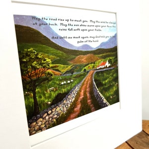 Puede incluir: Una pintura de acuarela de un camino sinuoso que conduce a una peque&ntilde;a caba&ntilde;a con techo rojo. El camino est&aacute; bordeado de muros de piedra y el paisaje circundante es verde y exuberante. La pintura incluye el texto: "Que el camino se eleve para encontrarte. Que el viento est&eacute; siempre a tu espalda. Que el sol brille c&aacute;lido sobre tus rostros, que la lluvia caiga suave sobre tus campos. Y hasta que nos encontremos de nuevo, que Dios te sostenga en la palma de su mano."
