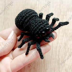 May include: A black crocheted spider with pink eyes. The spider is sitting on a person's hand.