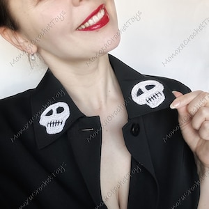 May include: A black blazer featuring two white crochet skull patches on the lapels. The skulls have black eyes and white teeth. The image is watermarked with the text "Monoxa Crochet Toys".