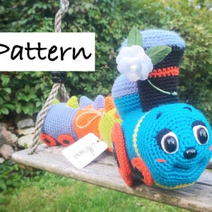 May include: A crocheted toy train with a blue engine, orange and green cars, and a white flower on top. The train is sitting on a wooden swing set.