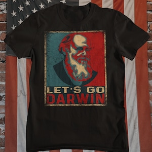 May include: A black t-shirt with a vintage-style image of Charles Darwin. The image is in red, white, and blue colors and has the text "Let's Go Darwin" below it.