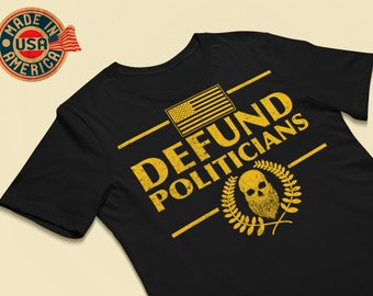 Peut inclure: T-shirt noir avec un motif graphique jaune qui dit "DEFUND POLITICIANS" avec un drapeau américain et un crâne avec une barbe dans une couronne de laurier.