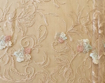 May include: Beige floral lace fabric with delicate embroidery. The lace features a repeating pattern of flowers and leaves in shades of pink, white, and light blue.