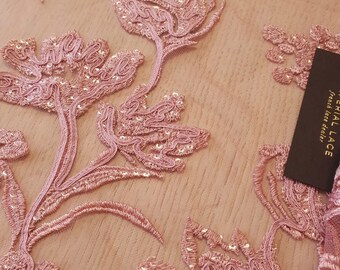 May include: Pink floral lace fabric with sequins. The fabric has a delicate, intricate design with a subtle shimmer.