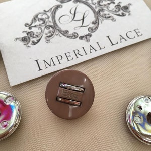 May include: A close-up of a brown plastic snap button with a silver metal insert that reads "EXE".